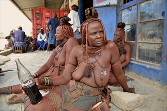 Traditionally dressed Himba woman drinking a coke in front of a bar, Opuwo, Kaokoland, Kunene,