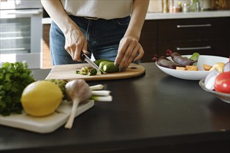 Close-up of female hands chopping fresh baby zucchini on wooden board