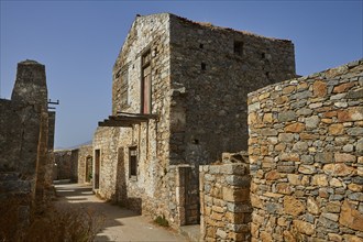 Old stone buildings in an abandoned village under clear skies with visible ruins, Venetian sea