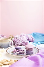 Purple macarons or macaroons cakes with cup of coffee on a white and pink background and