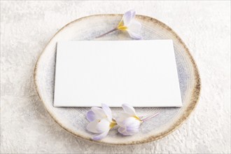 White paper invitation card, mockup with crocus flowers on ceramic plate and gray concrete