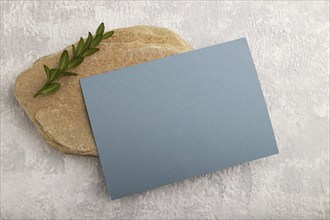 Blue paper business card, mockup with natural stone and boxwood branch on gray concrete background.