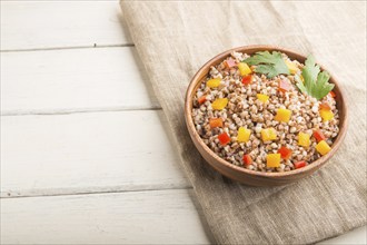 Buckwheat porridge with vegetables in wooden bowl on a white wooden background and linen textile.