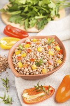 Buckwheat porridge with vegetables in clay bowl on a gray concrete background and linen textile.