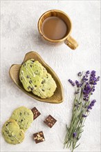 Green cookies with chocolate and mint on leaflike ceramic plate with cup of coffee on gray concrete