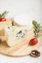 Blue cheese and various types of cheese with rosemary and tomatoes on wooden board on a white