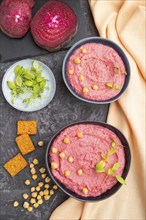 Hummus with beet and microgreen basil sprouts in ceramic bowl on a black concrete background and