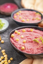 Hummus with beet and microgreen basil sprouts in ceramic bowl on a black concrete background and