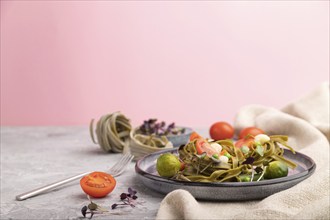 Tagliatelle green spinach pasta with tomato, pea and microgreen sprouts on a gray and pink