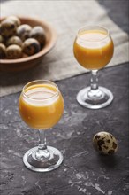 Sweet egg liqueur in glass with quail eggs on a black concrete background. Side view, low key,