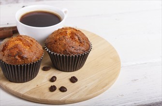 Two carrot muffins with cup of coffee on wooden kitchen board on white wooden background with