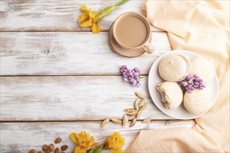 Meringues cakes with cup of coffee on a white wooden background and orange linen textile. Top view,