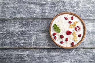 Rice flakes porridge with milk and strawberry in wooden bowl on gray wooden background. Top view,