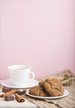 Homemade oatmeal cookies with a cup of cocoa on a linen textile and pink pastel background. side