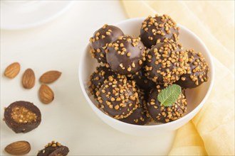 Chocolate caramel ball candies with almonds and a cup of coffee on a white wooden background and