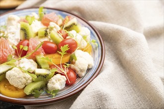 Vegetarian salad of cauliflower cabbage, kiwi, tomatoes, microgreen sprouts on black concrete