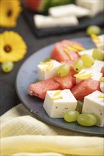 Vegetarian salad with watermelon, feta cheese, and grapes on blue ceramic plate on black concrete