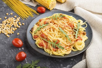 Corn noodles with tomato sauce and arugula on a black concrete background and linen textile. Side