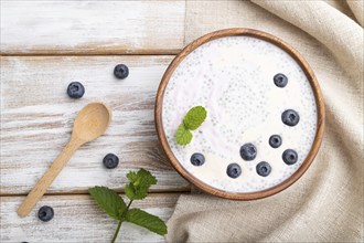 Yogurt with blueberry in wooden bowl on white wooden background and linen textile. top view, flat