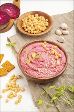 Hummus with beet and microgreen basil sprouts in wooden bowl on a white wooden background and linen