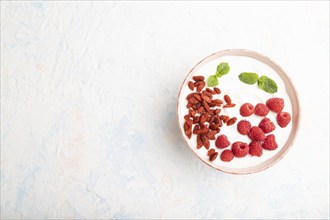 Yogurt with raspberry and goji berries in ceramic bowl on white concrete background. top view, flat