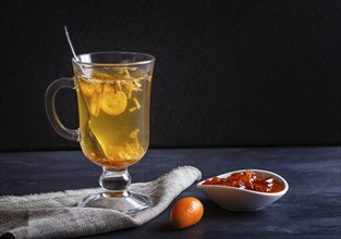 Jasmine tea with kumquat in a glass cup on a wooden board on a black background. close up, copy