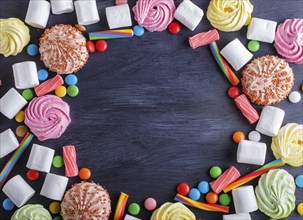 Colorful frame of multicolored candies on black wooden background. Circle copy space, top view,