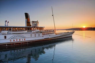 Anchored steamship Savoie backlit at sunrise in the mirror-smooth Geneva harbour basin, Canton of