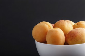 Fresh orange apricots in white bowl on black background. side view, close up, selective focus