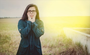 Portrait of beautiful woman with glasses in the field. Cute Girl in glasses with hands on cheeks