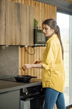 Young woman frying vegetables in a pan in the kitchen using electric stove