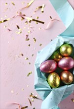 Small chocolate Easter eggs wrapped in shiny foil, placed on a bed of shredded pastel-colored