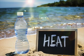 Water bottle next to chalkboard with text 'heat' at beach. KI generiert, generiert, AI generated