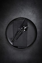 Food background, with an empty black plate, black cutlery, with a napkin, on a black background,