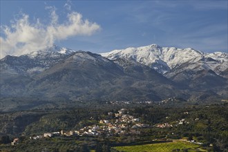 Small village in hilly landscape under snow-capped mountains and blue sky, vineyard, olive groves,