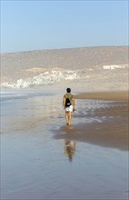 Man walking barefoot on sandy beach at low tide near village of Taghazout, Morocco, North Africa,