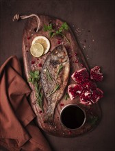 Fried dorado fish, with spices and herbs, on a wooden board, pomegranate sauce, close-up, no people