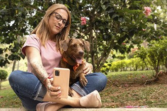 Middle-aged woman in jeans and reading glasses tries to take a selfie with her dog who looks away