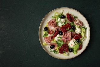 Salad with dried tomatoes, prosciutto, soft cheese, olives, homemade, top view