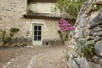 Natural stone wall with a red spur flower (Centranthus ruber) and old house with a door and roof in