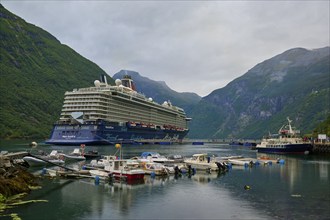 A large cruise ship, my ship 6, lies in the harbour of a fjord, surrounded by smaller boats and