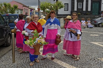 Women in colourful traditional dress stand on a street and smile, Fenais da Luz, Sao Miguel Island,