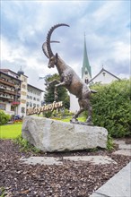 Bronze statue of a rising goat in front of a church and buildings in the background, Mayrhofen,