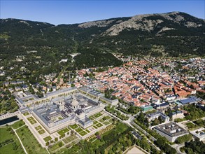 Large historic monastery and surrounding town in a green and mountainous landscape, taken from the