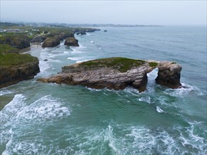 A striking rock in the shape of a natural bridge, surrounded by foaming waves and a tantalising