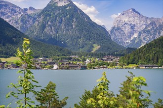 Lake surrounded by green mountains with a small cluster of houses in the sunlight, Achernsee,