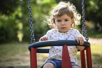 Child, 2 years, swings outdoors in a playground with a sunny atmosphere