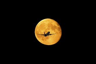 PHOTOMONTAGE, silhouette of an aeroplane flying in front of a glowing full moon in the night sky