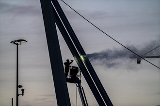 Worker cleans a bridge pier with a high-pressure cleaner on a cherry picker at the Erasmus Bridge