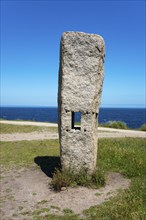 Single upright stone with square opening, in the background the sea and blue sky, Menhires por la